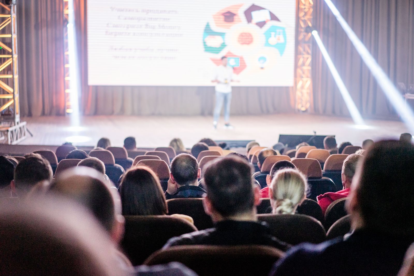 Audience watching a presentation in a conference hall with stage lighting