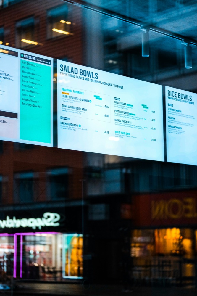 Digital menu board displaying salad and rice bowls in a restaurant window